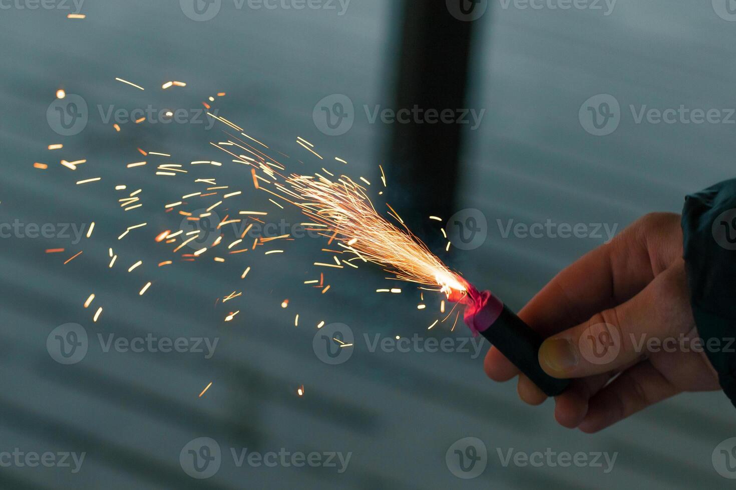 Burning Firecracker with Sparks. Guy Holding a Petard in a Hand. Loud and Dangerous New Year's Entertainment. Hooliganism with Pyrotechnics. Noise of Firecrackers in Public Places photo