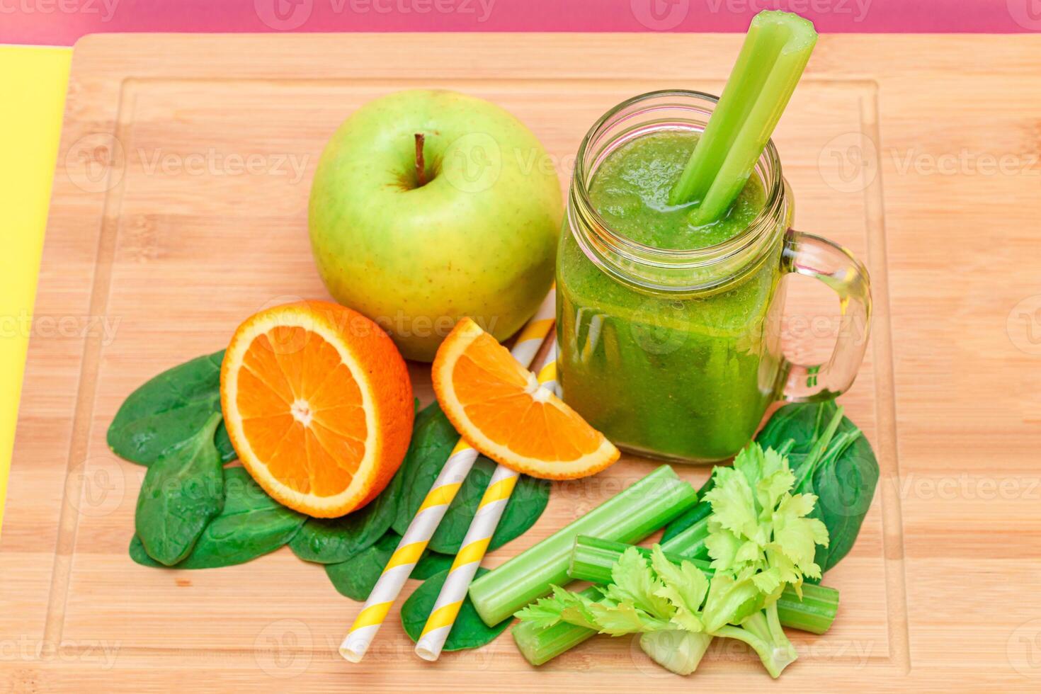 Fresh Green Smoothie of Apple, Celery, Spinach and Orange in Glass Smoothie Jar with Yellow Cocktail Straw on Wooden Cutting Board. Vegan Detox Drink. Vegetarian Culture. Healthy Eating and Fruit Diet photo