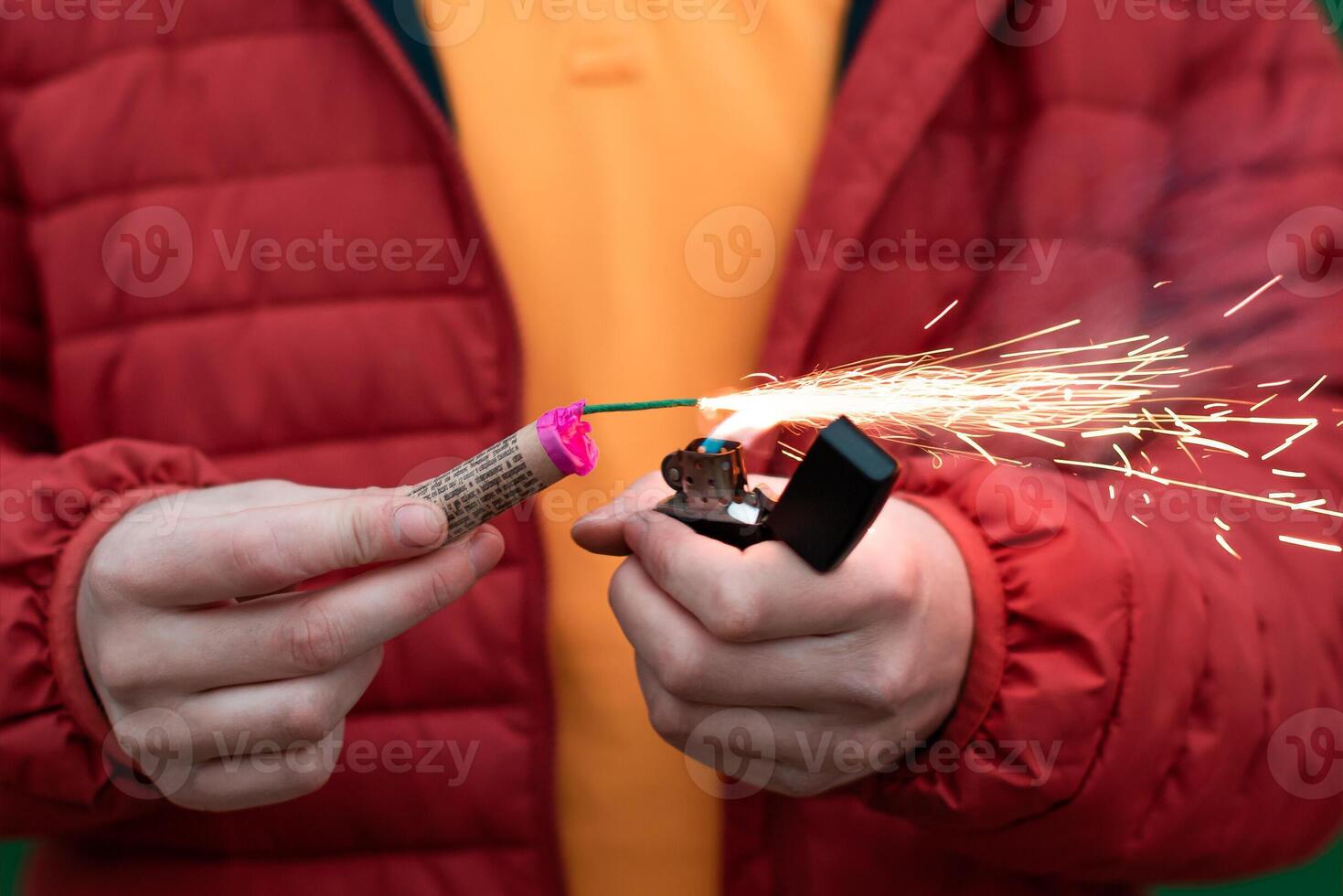 Man in Red Jacked Lighting Up Firecracker in his Hand Using Gasoline Lighter. Guy Getting Ready for New Year Fun with Fireworks or Pyrotechnic Products photo