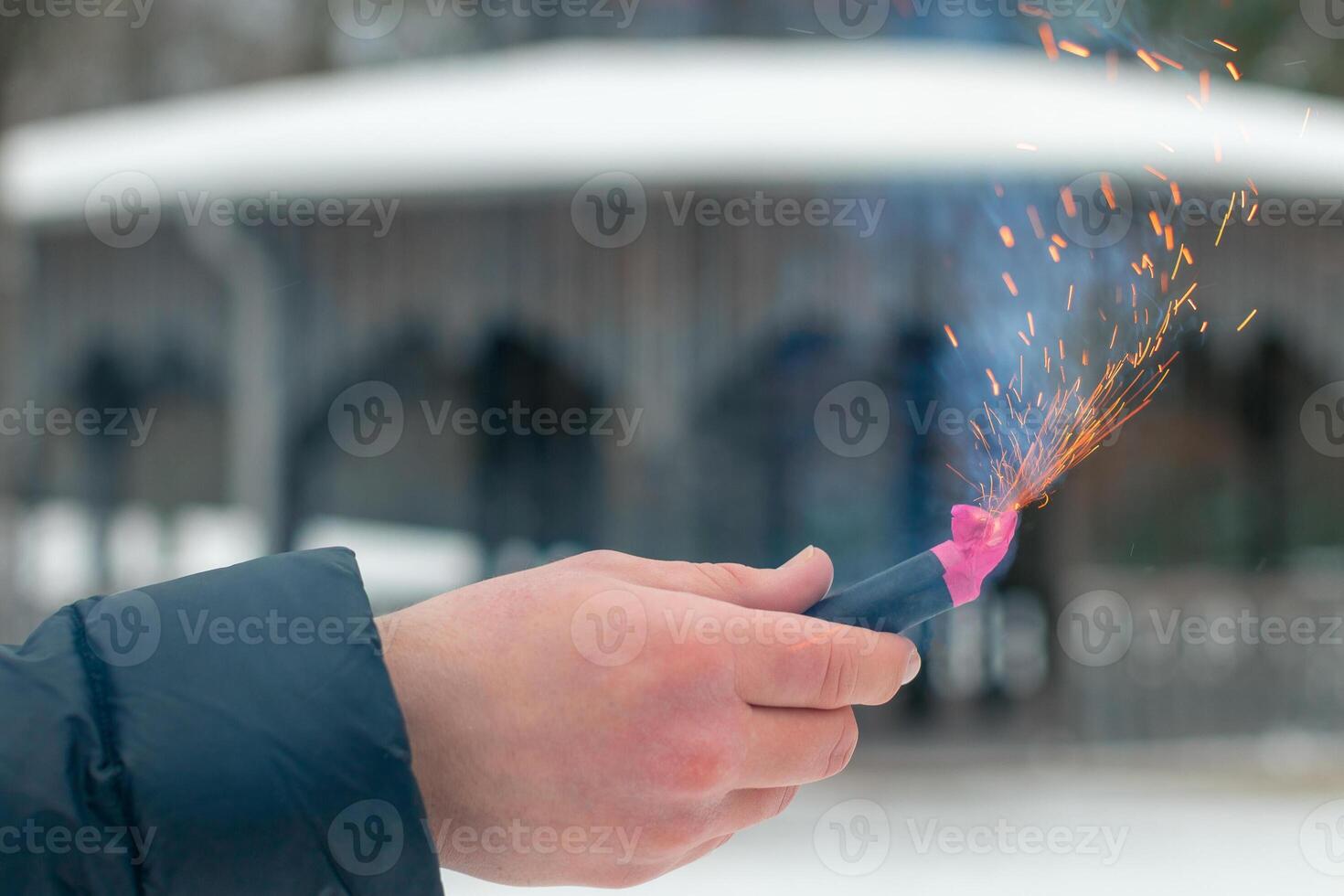 Burning Firecracker in a Hand. Guy Holding a Petard Outdoors in Winter at Daytime. Loud and Dangerous New Year's Entertainment. Hooliganism with Pyrotechnics. Noise of Firecrackers in Public Places photo