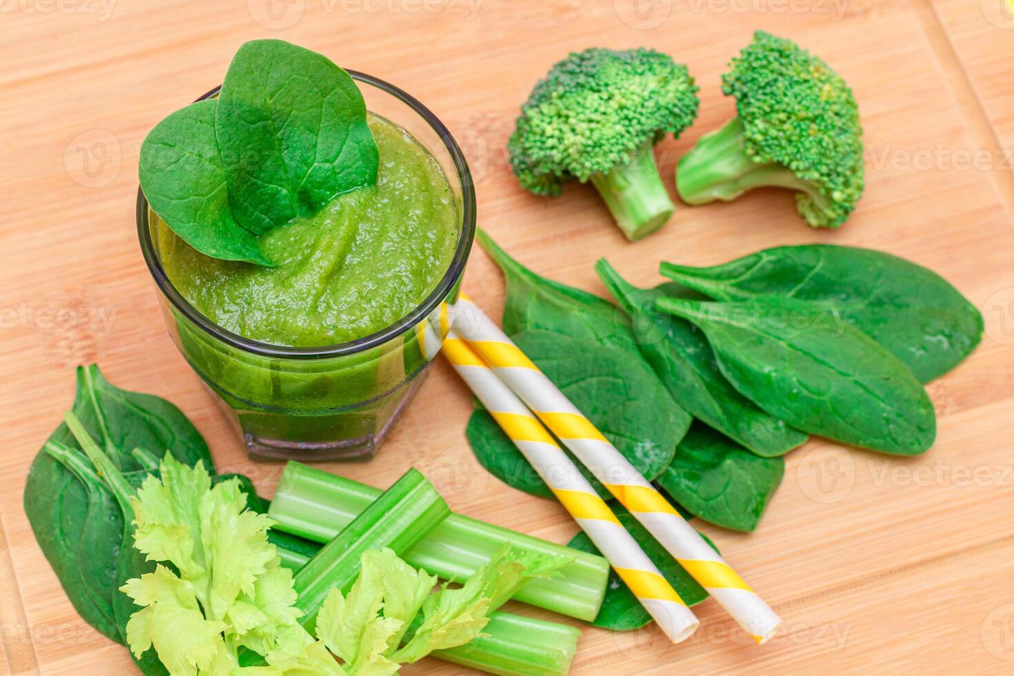 Fresh Green Smoothie of Apple, Celery, and Spinach in Glass Beaker with Yellow Cocktail Straw on Wooden Cutting Board. Vegan Detox Drink. Vegetarian Culture. Healthy Eating and Fruit Diet photo