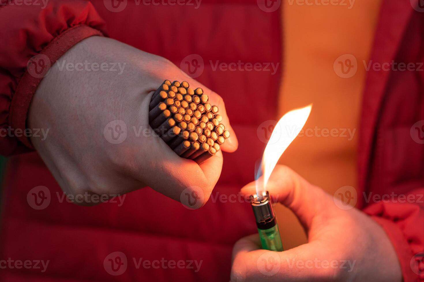 Man in Red Jacked Lighting Up Many Small Black Firecrackers in his Hand Using Gas Lighter. Guy Getting Ready for New Year Fun with Fireworks or Pyrotechnic Products photo