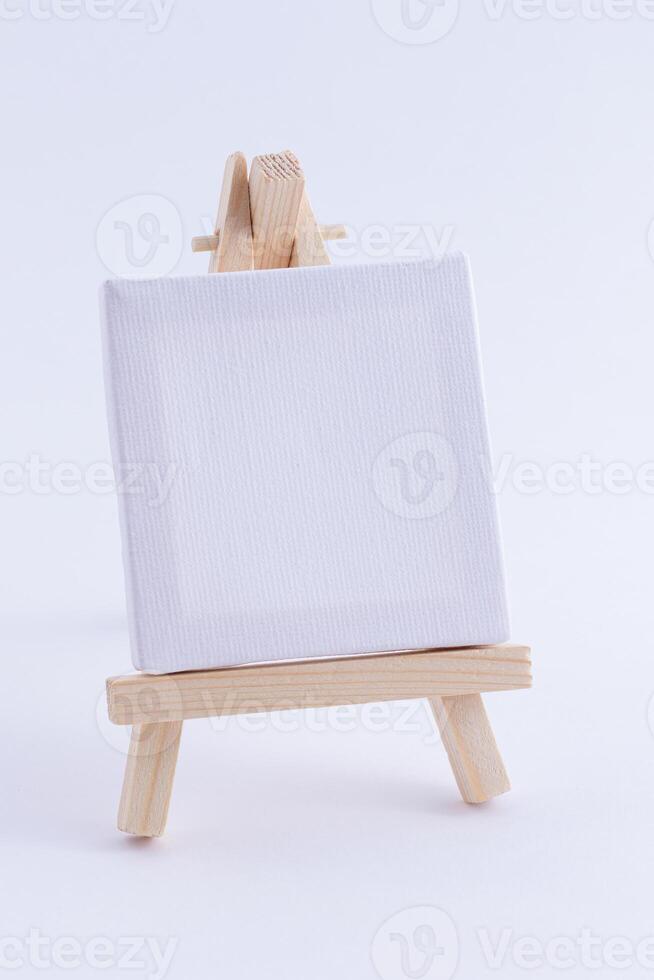 Wooden Easel Miniature with Blank White Square Canvas for Artists and Painters - Mockup. Mini Wooden Stand with Clean Artboard on White Background, Copy Space photo