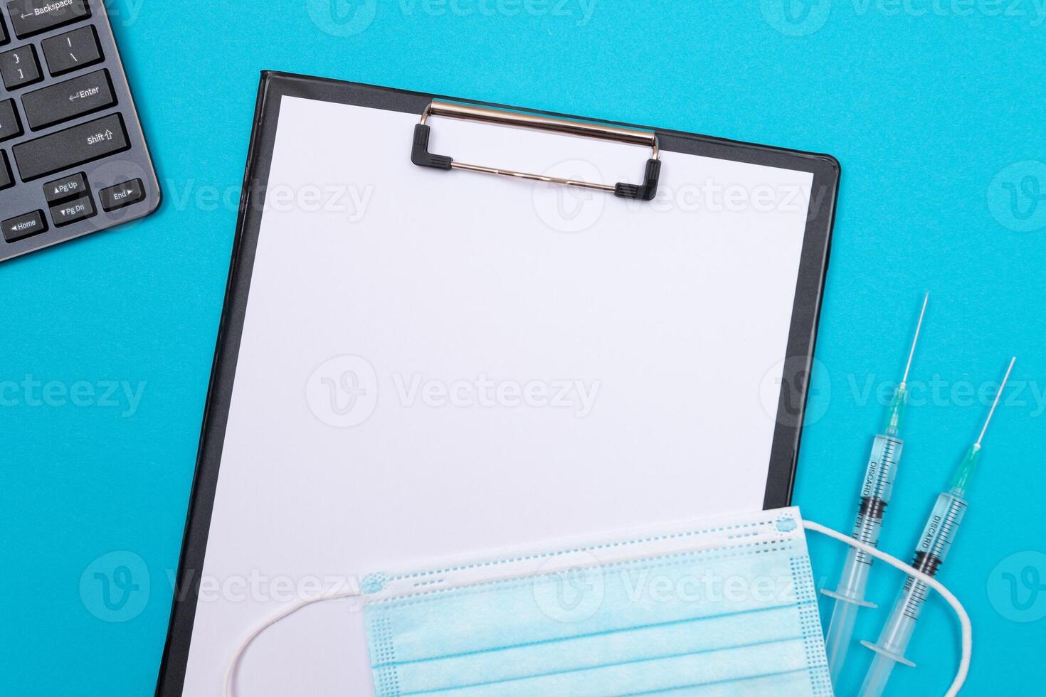 Vaccination, Immunology or Revaccination Concept - Two Medical Syringe Lying on Blue Table in Doctor's Office in a Hospital or Clinic. Black Clipboard with Sheet of Paper - Mock Up with Copy Space photo