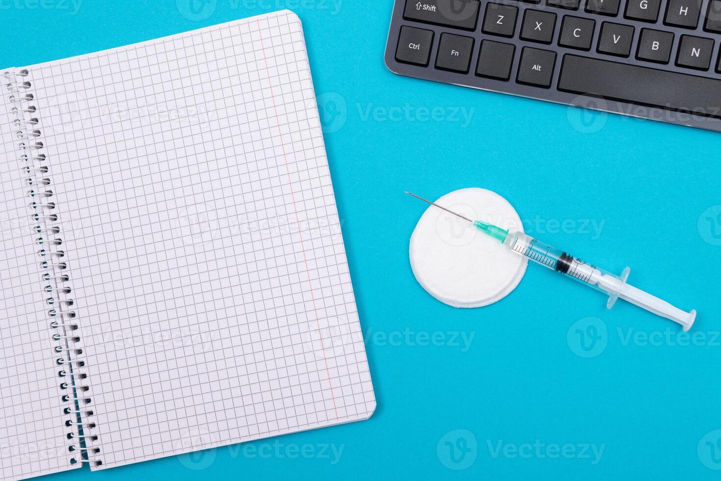 Vaccination, Immunology or Revaccination Concept - A Medical Syringe Lying on Blue Table in Doctor's Office in a Hospital or Clinic. Opened Blank Notepad - Mock Up with Copy Space photo