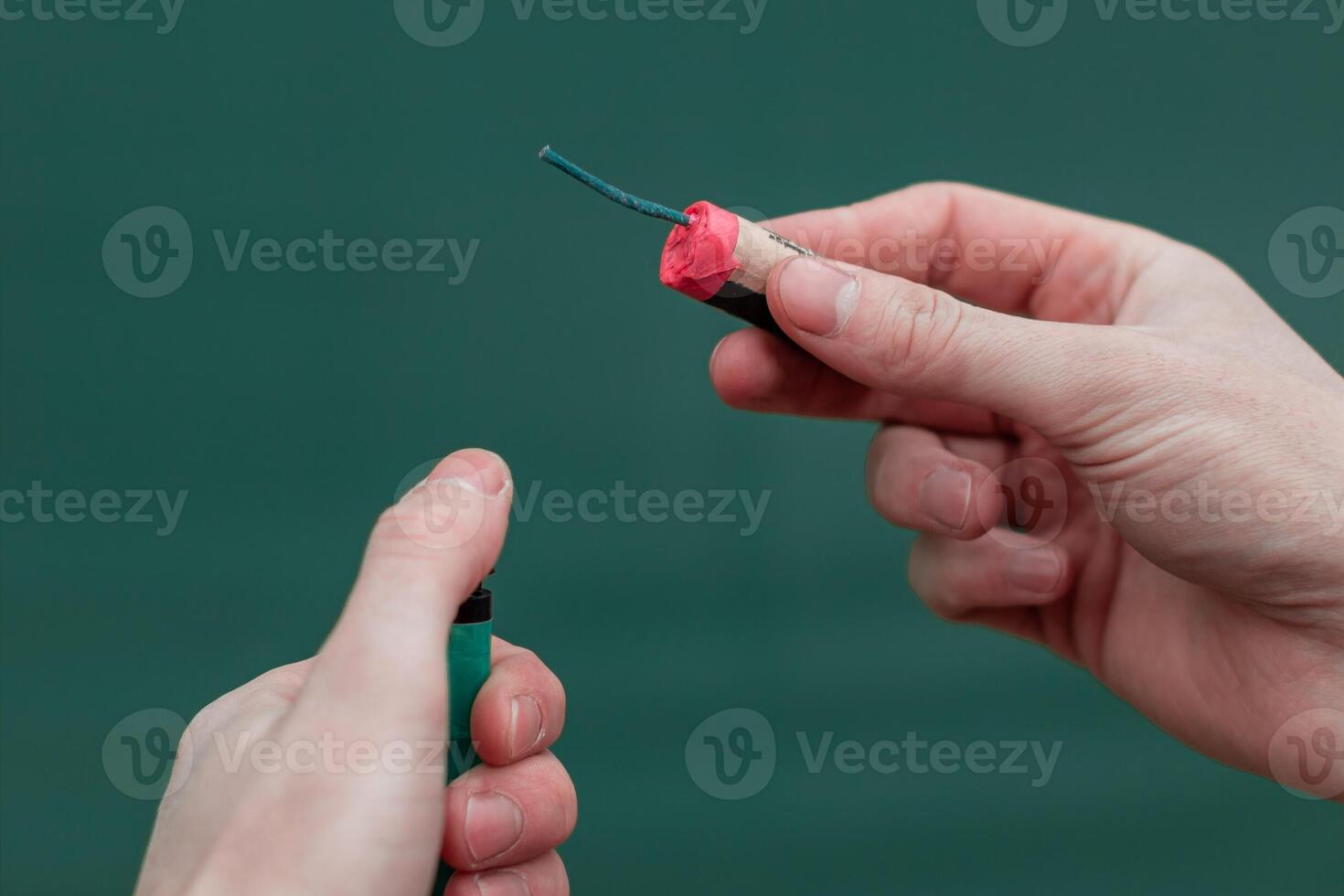 Man Lighting Up Firecracker in his Hand Against the Blue Background Using Gas Lighter photo