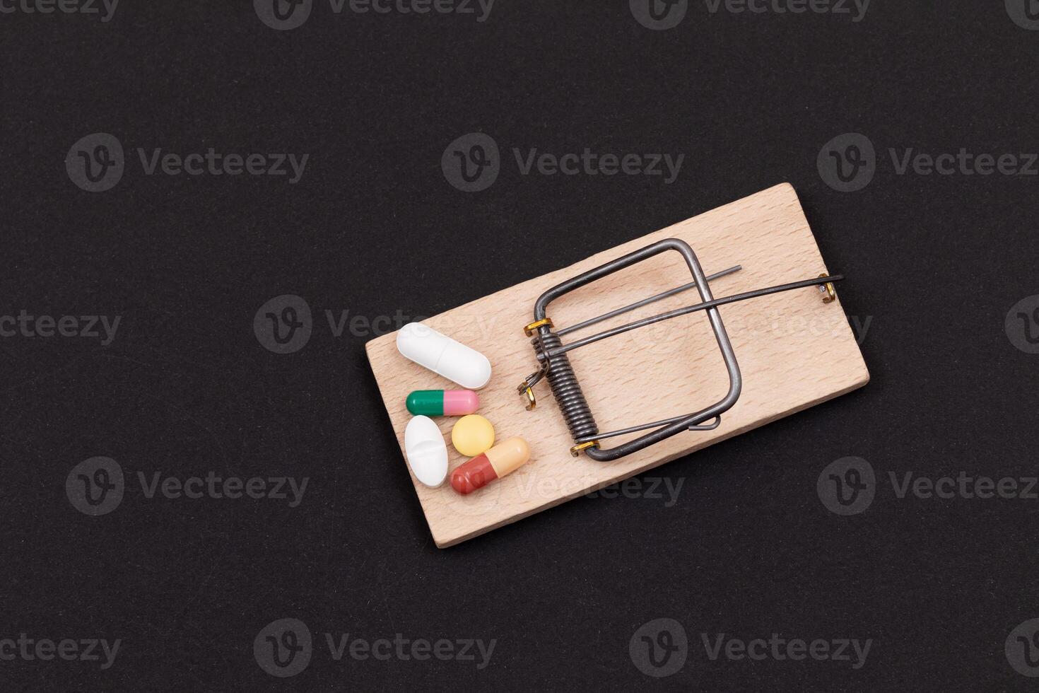 Pharmaceutical Addiction or Big Pharma Trap - Colored Pills or Capsules in Wooden Mousetrap on Black Background photo