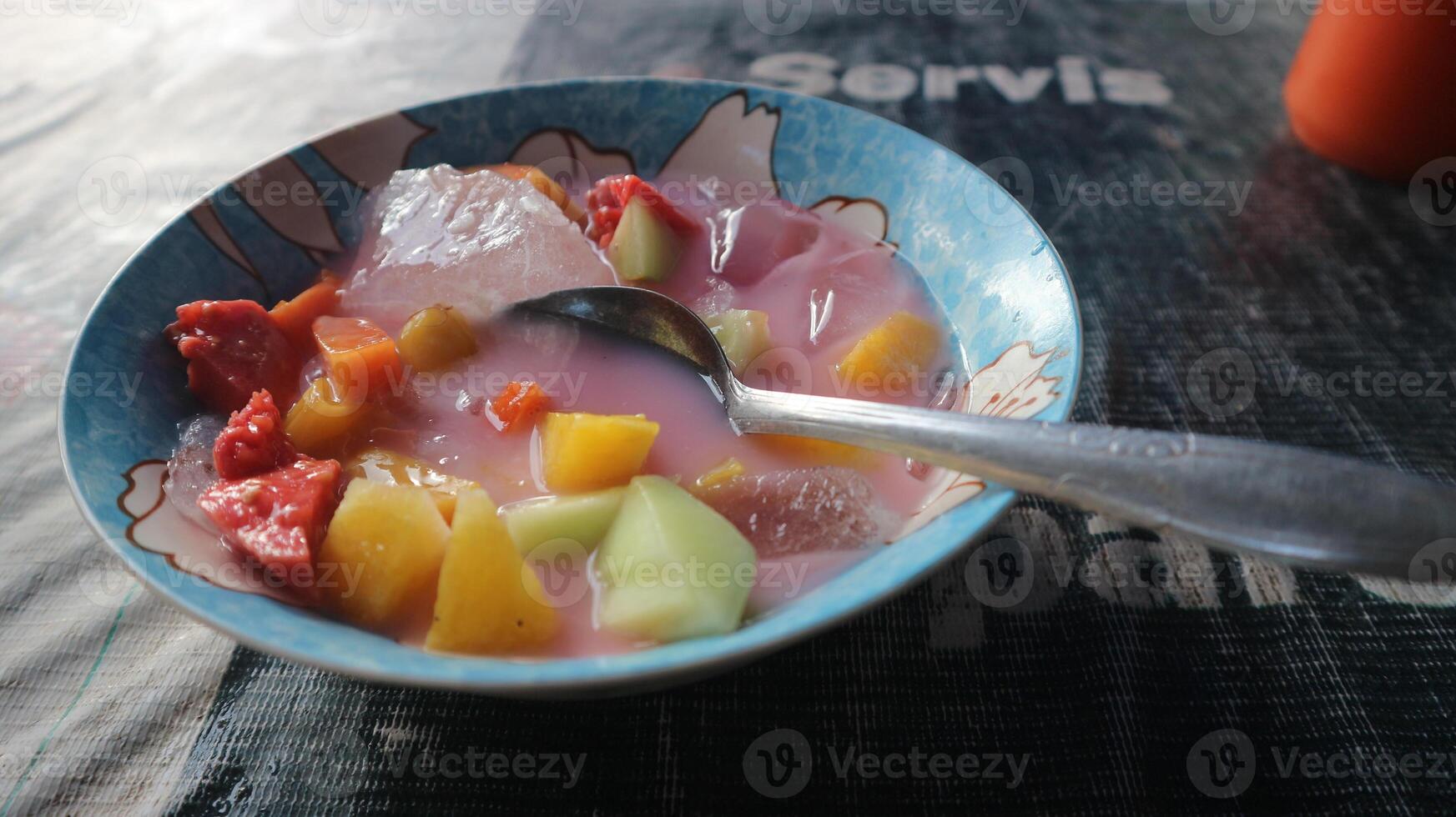 sop buah or fruit soup is indonesian fruit cocktail ice made from various diced fruits mixed with ice cubes, condensed milk and red syrup. popular for buka puasa break fasting. selected focus photo
