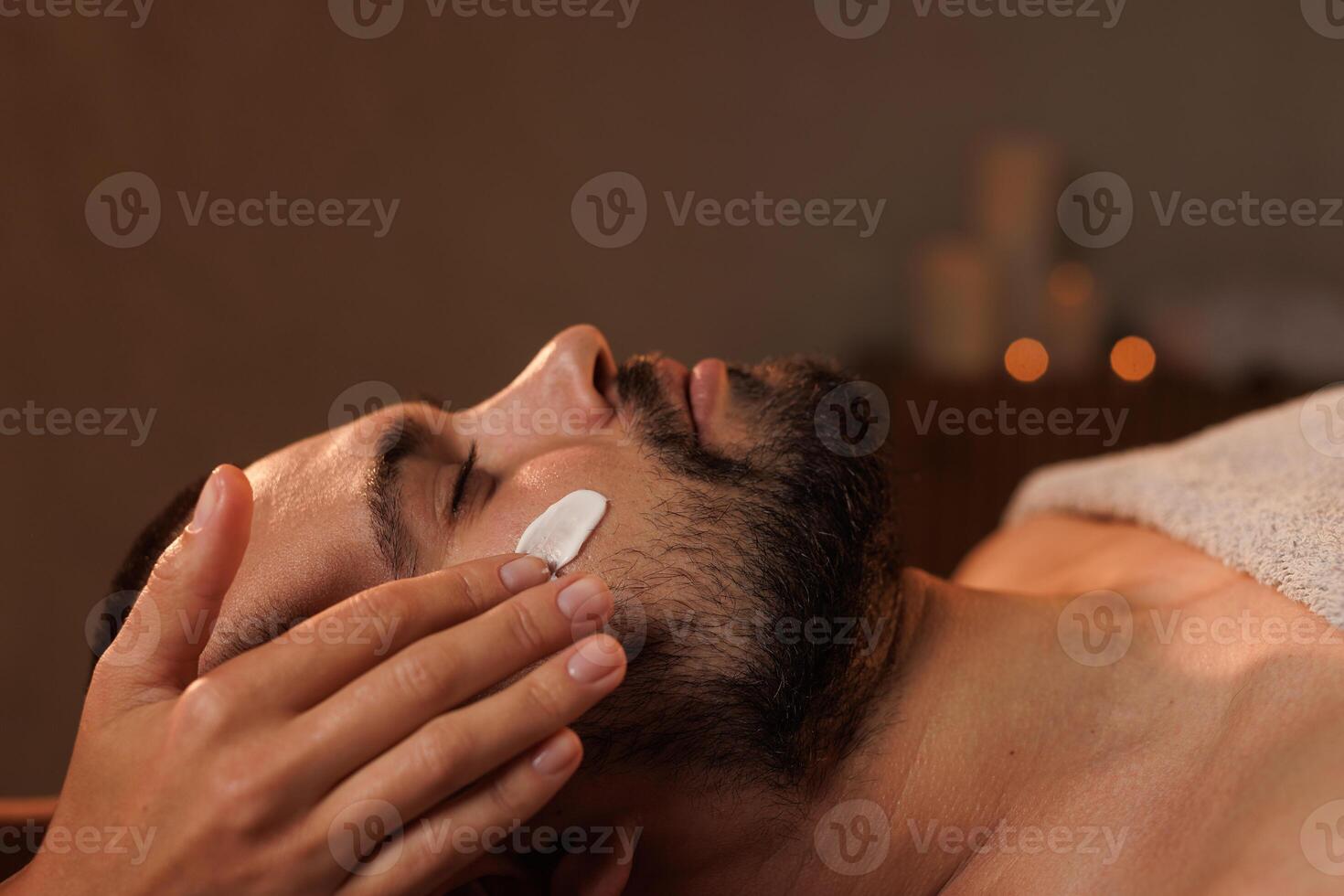 Cosmetician applying cosmetic cream of man in spa photo