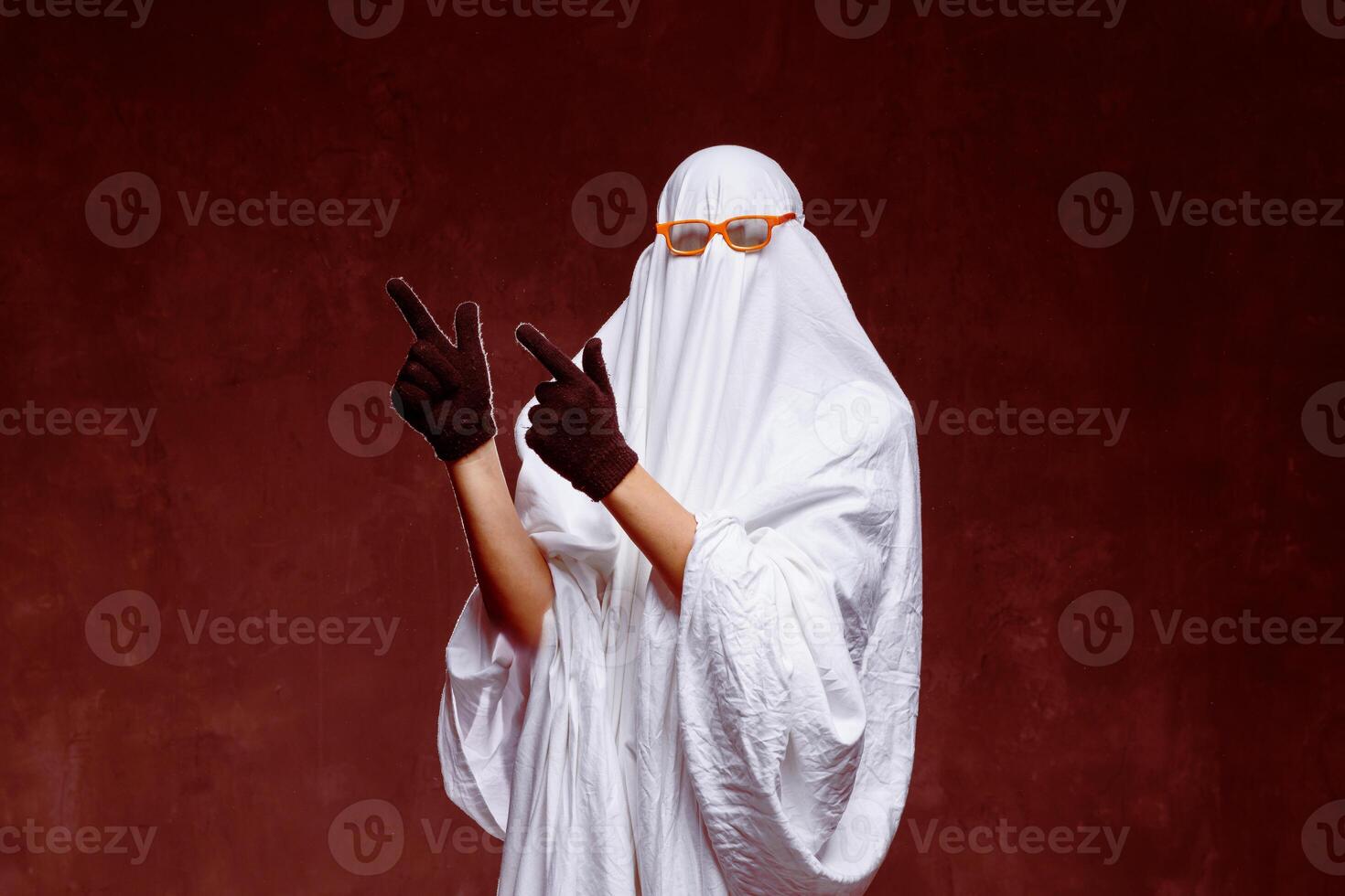 Man in ghost costume pointing at something on gray background in smoke with space for text. Halloween celebration photo