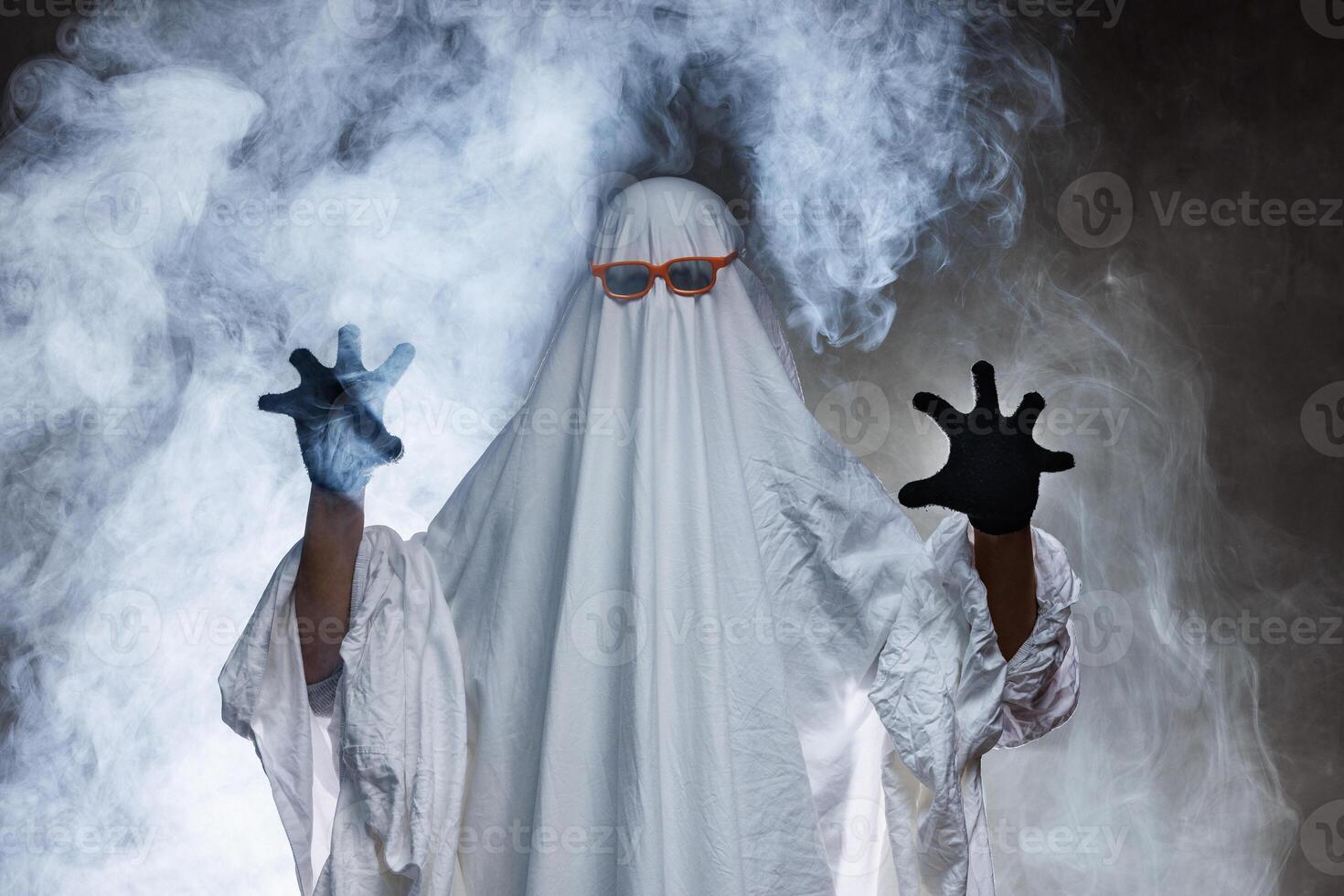 man in scary ghost costume in smoke on grey mysterious background in studio. Minimal halloween ghost concept. photo