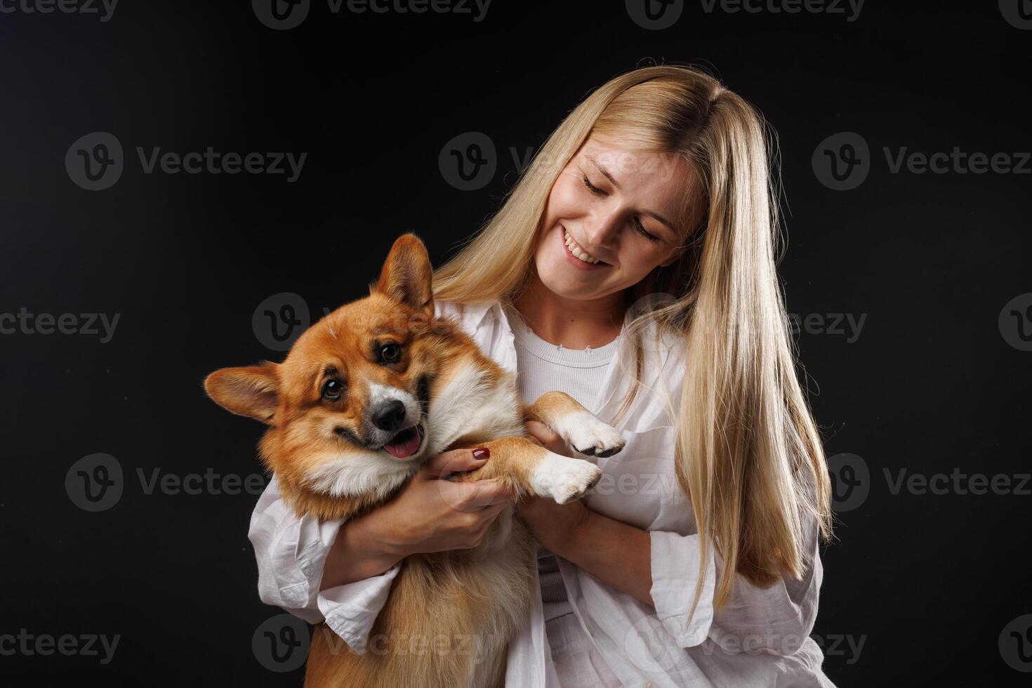 Woman holding and hugging happy corgi dog on black background. photo