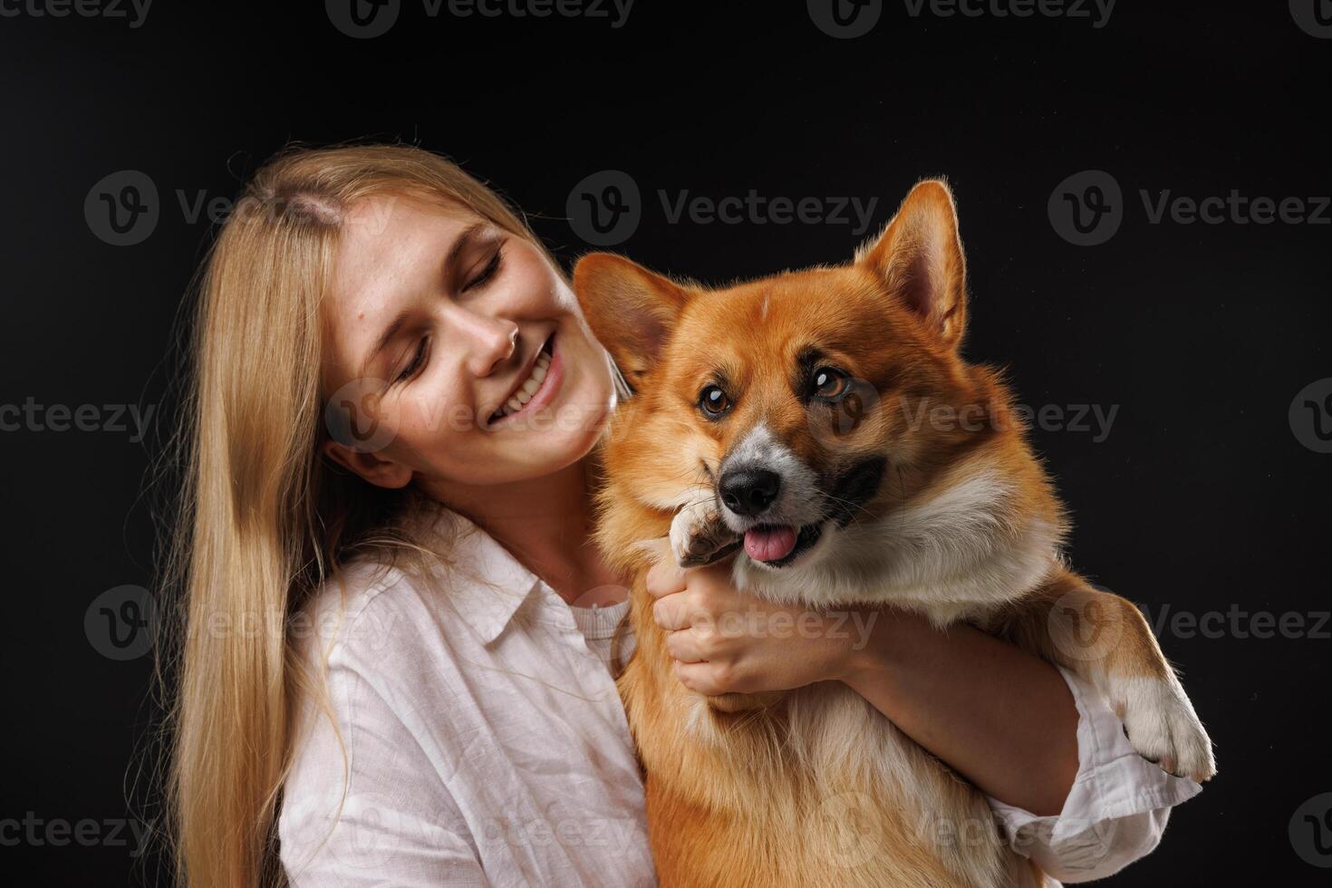 Woman holding and hugging happy corgi dog on black background. photo