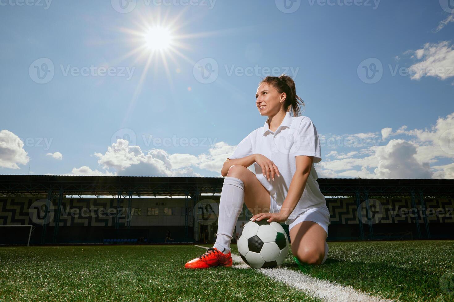 girl Football player in white shorts and red boots sets a soccer ball on a green field photo