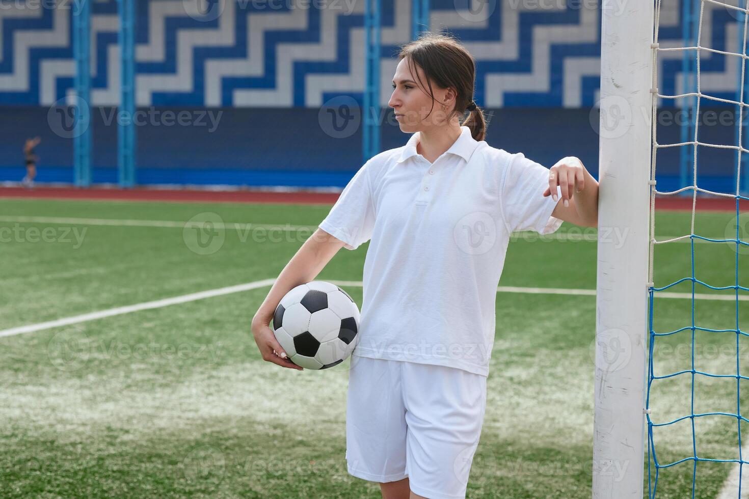 A female soccer player holds a soccer ball and leans against a goal post on a soccer field. photo