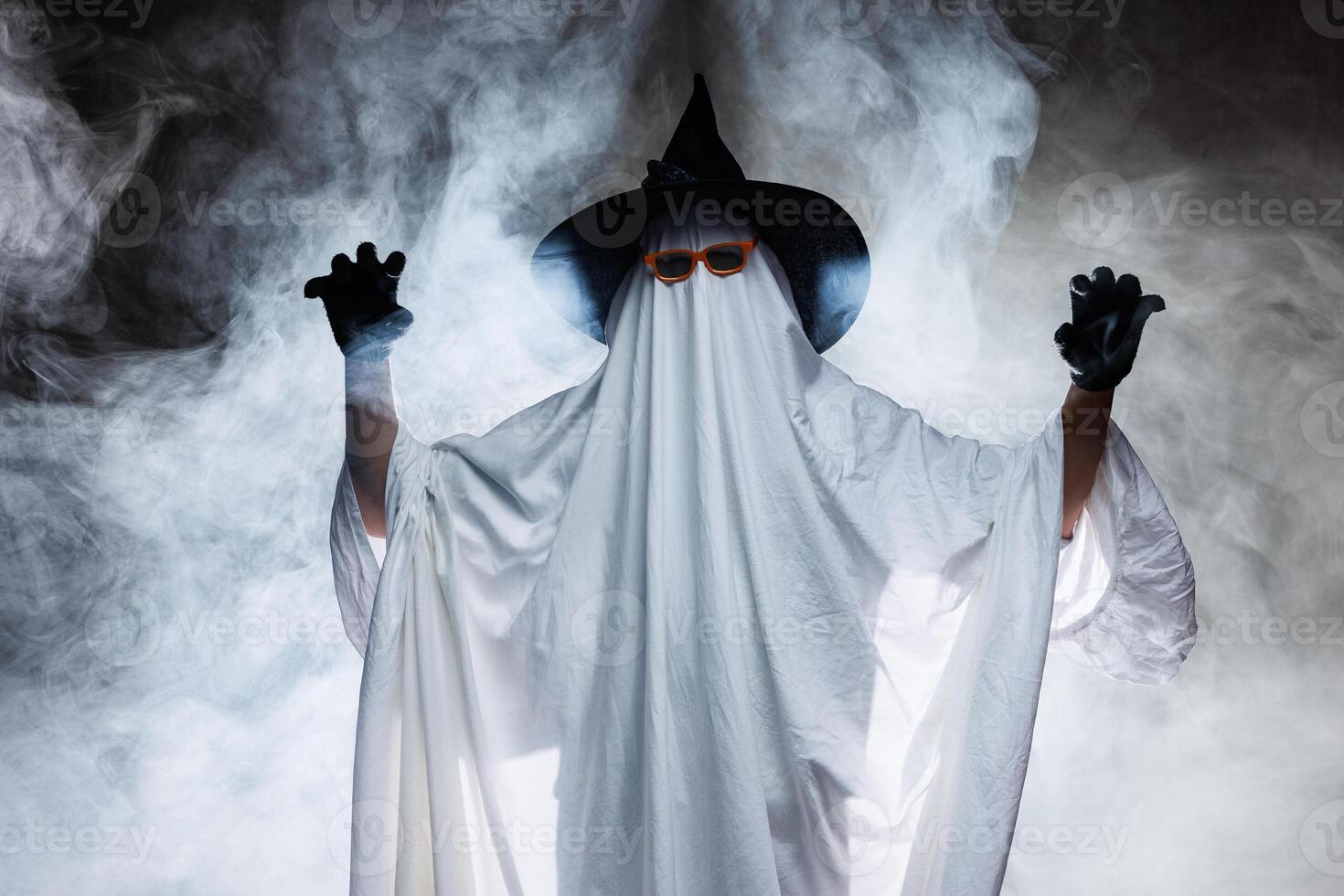 Man in scary ghost costume for Halloween and witch hat on dark mystical background in smoke photo