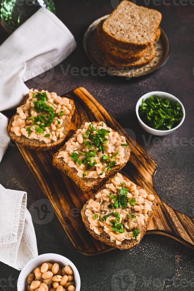 Bruschetta with mashed white beans and parsley on rye bread on a board vertical view photo