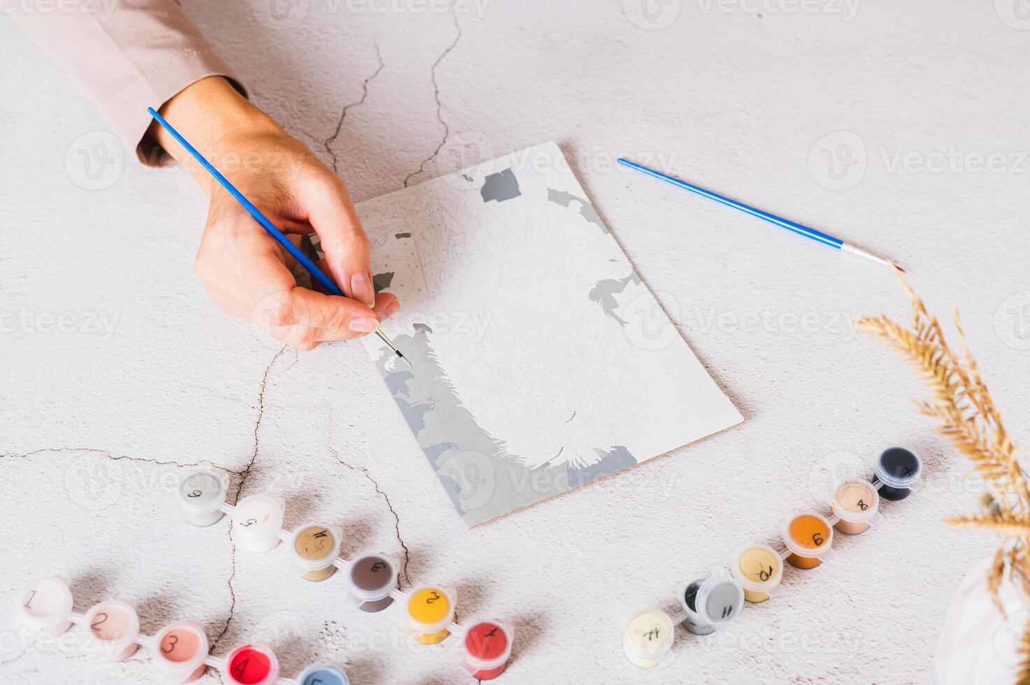 A woman's hand paints a picture by numbers on a table with a brush photo