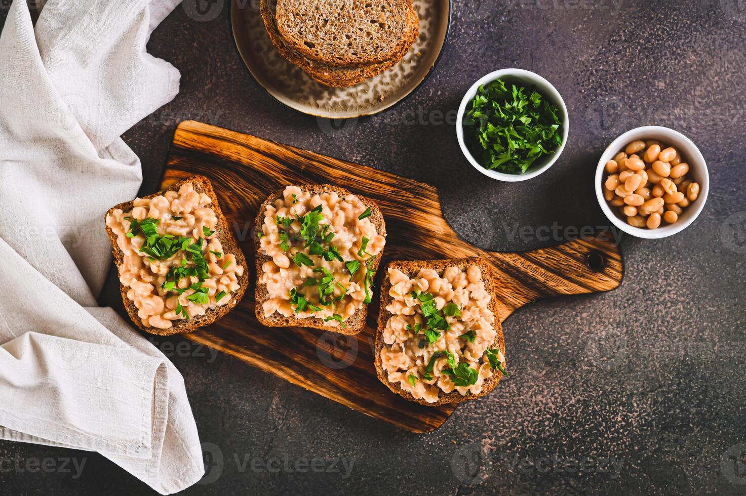 Appetizing sandwiches on grain bread with mashed beans and greens on a board top view photo