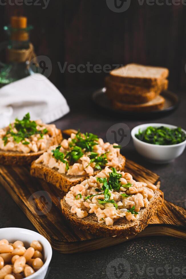 Appetizing sandwiches on grain bread with mashed beans and greens on a board vertical view photo