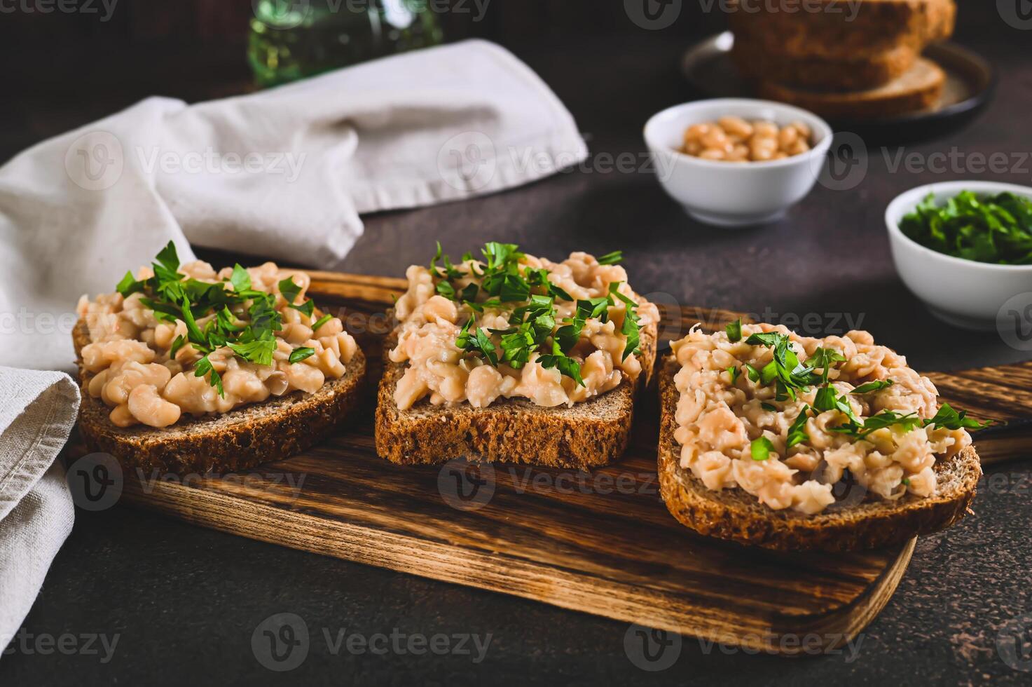 Appetizing sandwiches on grain bread with mashed beans and greens on a board on a table photo