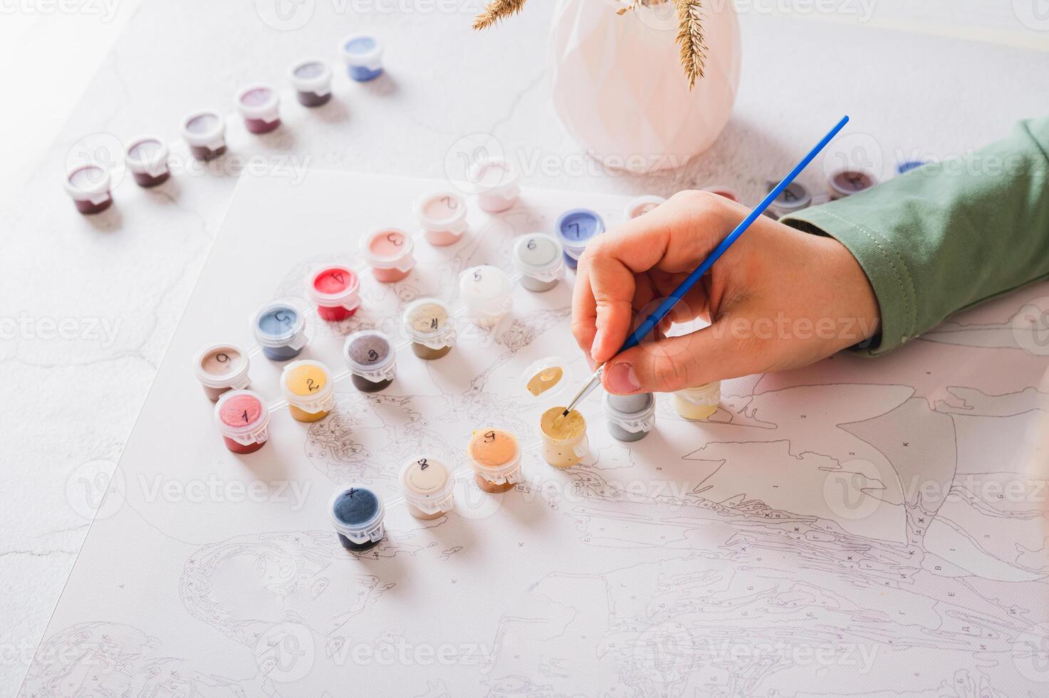Girl's hand dipping brush into paint to paint by numbers picture on table photo
