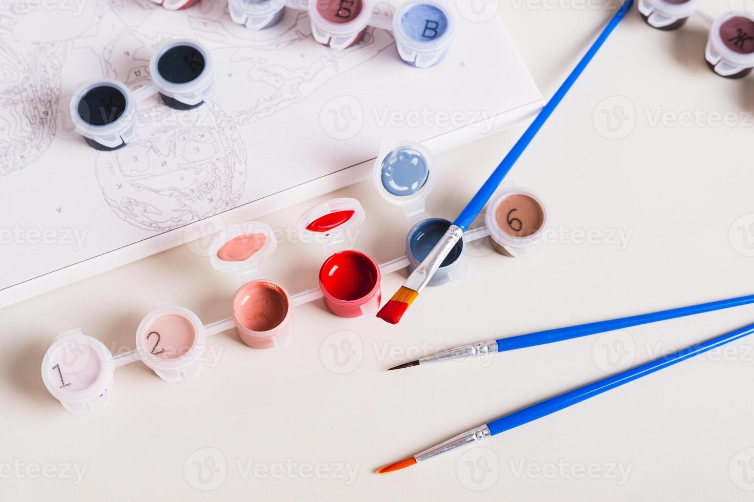 Brush dipped in red acrylic paint and containers with paints for painting a picture photo