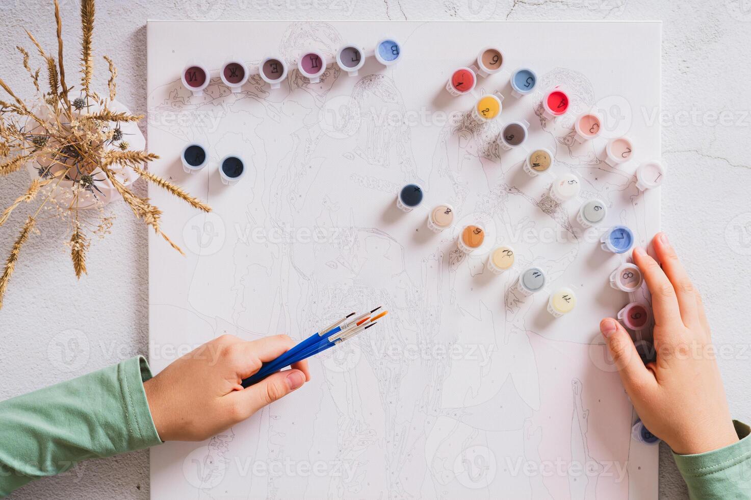 Girl's hands holding brushes and paints for painting by numbers top view photo