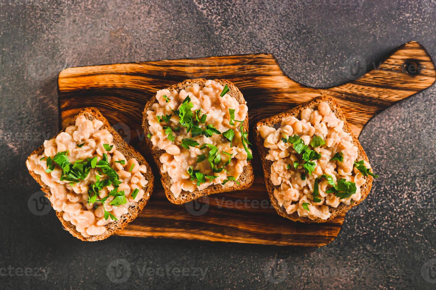 Close up of sandwiches on grain bread with mashed beans and greens on a board top view photo