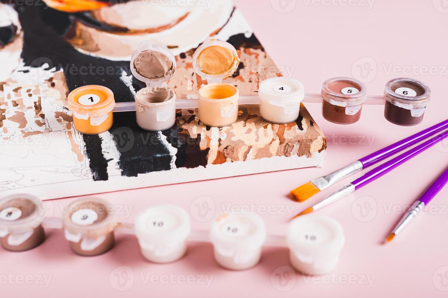 Open containers of paints and brushes for painting by numbers on pink background photo