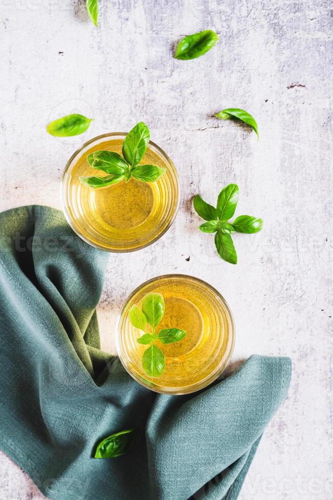 Refreshing summer basil lemonade with leaves in glasses on table top and vertical view photo