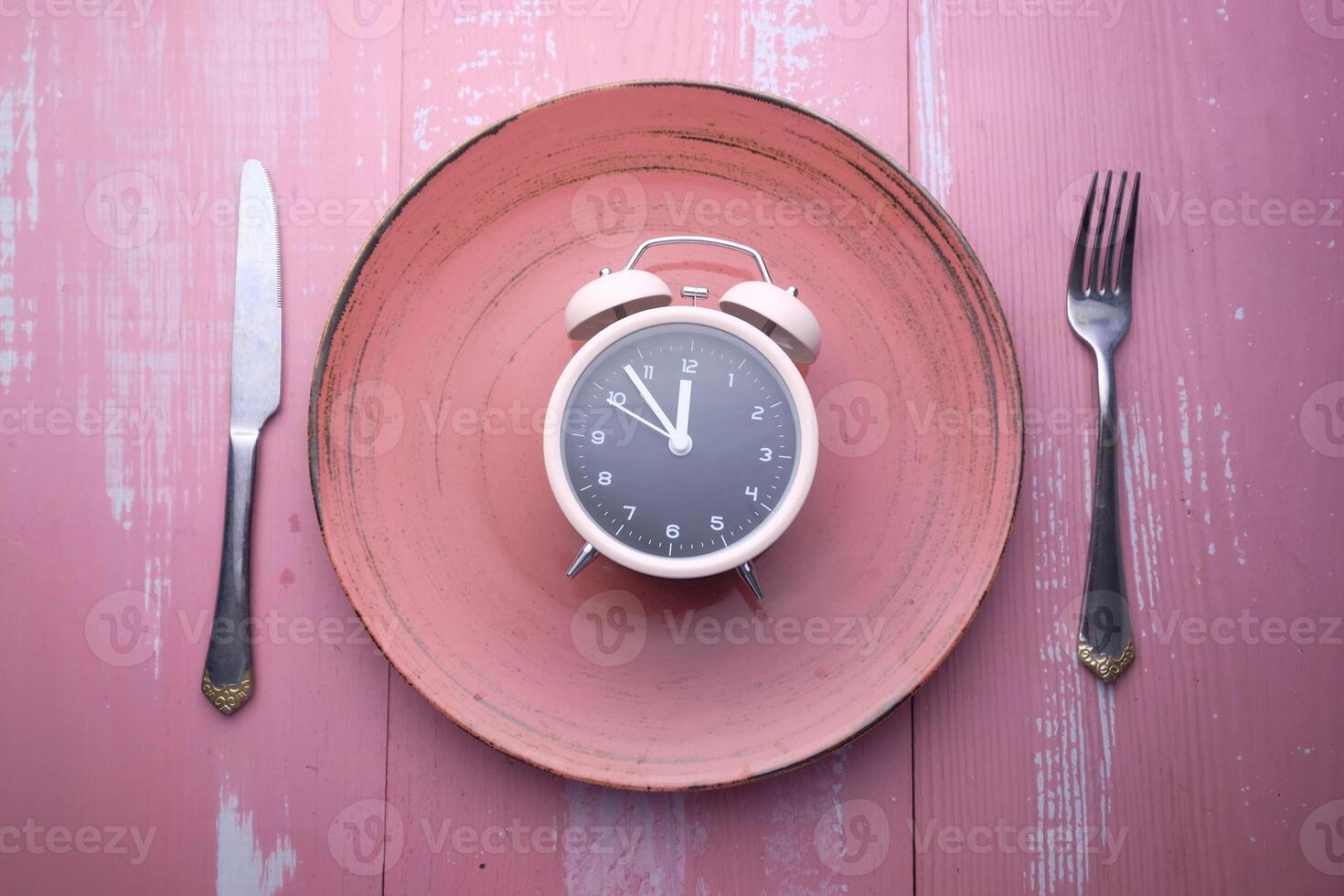 A beautifully designed clock on a plate with cutlery symbolizes the essence of mealtime photo