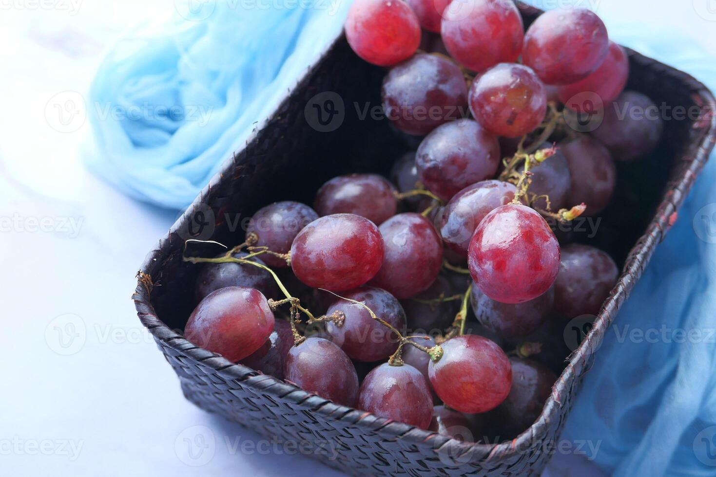 A beautiful arrangement of Fresh Red Grapes placed in a rusticlooking basket on blue cloth photo