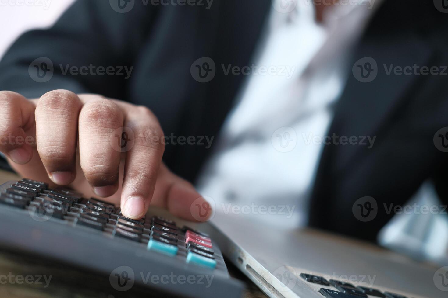 A Professional Engaged in Using a Calculator at a Desktop with a Laptop for Financial Analysis photo