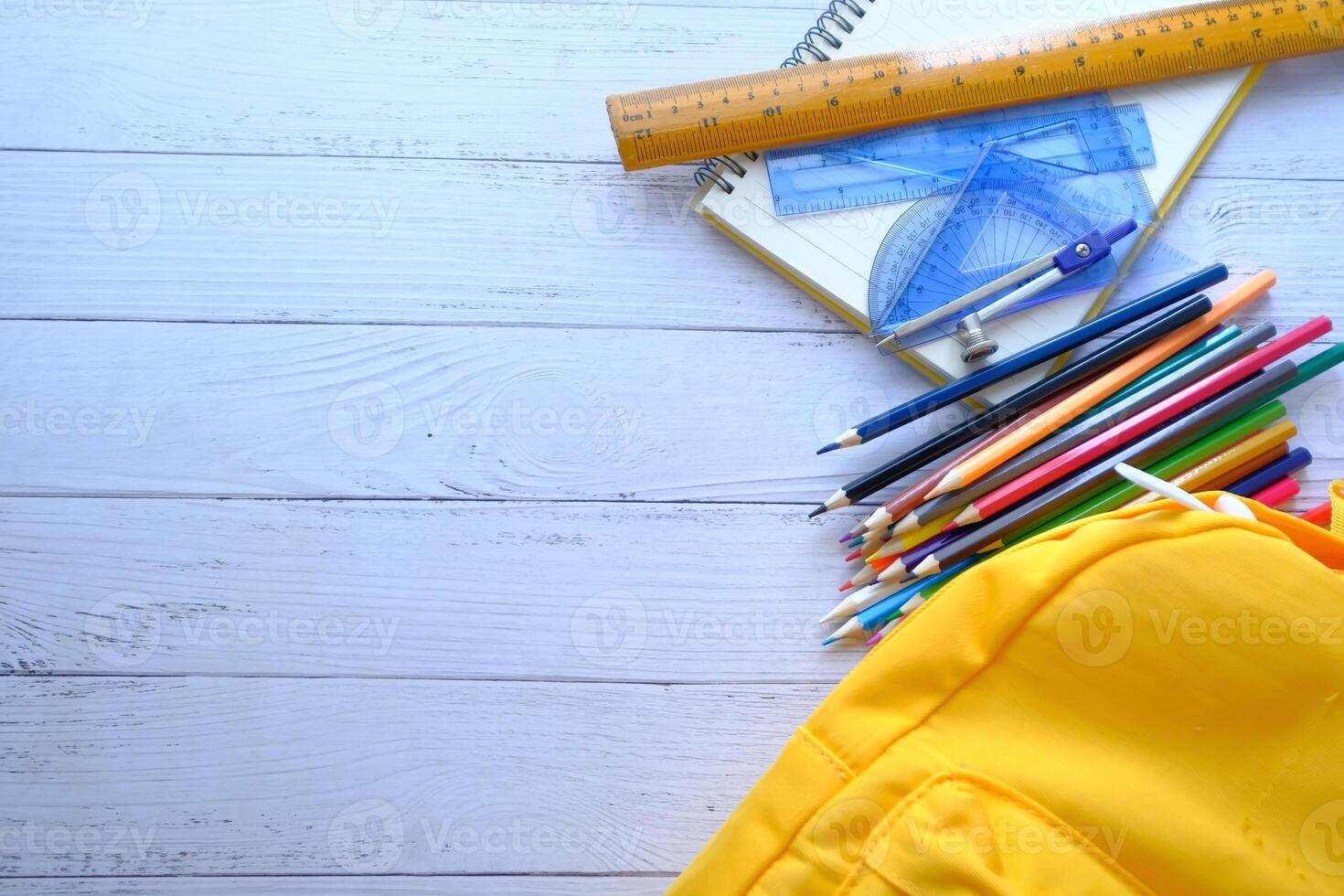 A Variety of Colorful School Supplies Spread Out on a Wooden Table Next to a Yellow Backpack photo