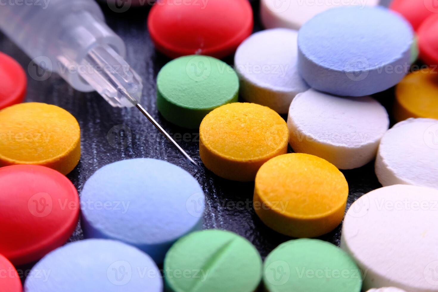 A Colorful Assortment of Various Pills and a Syringe Displayed on a Dark Background photo