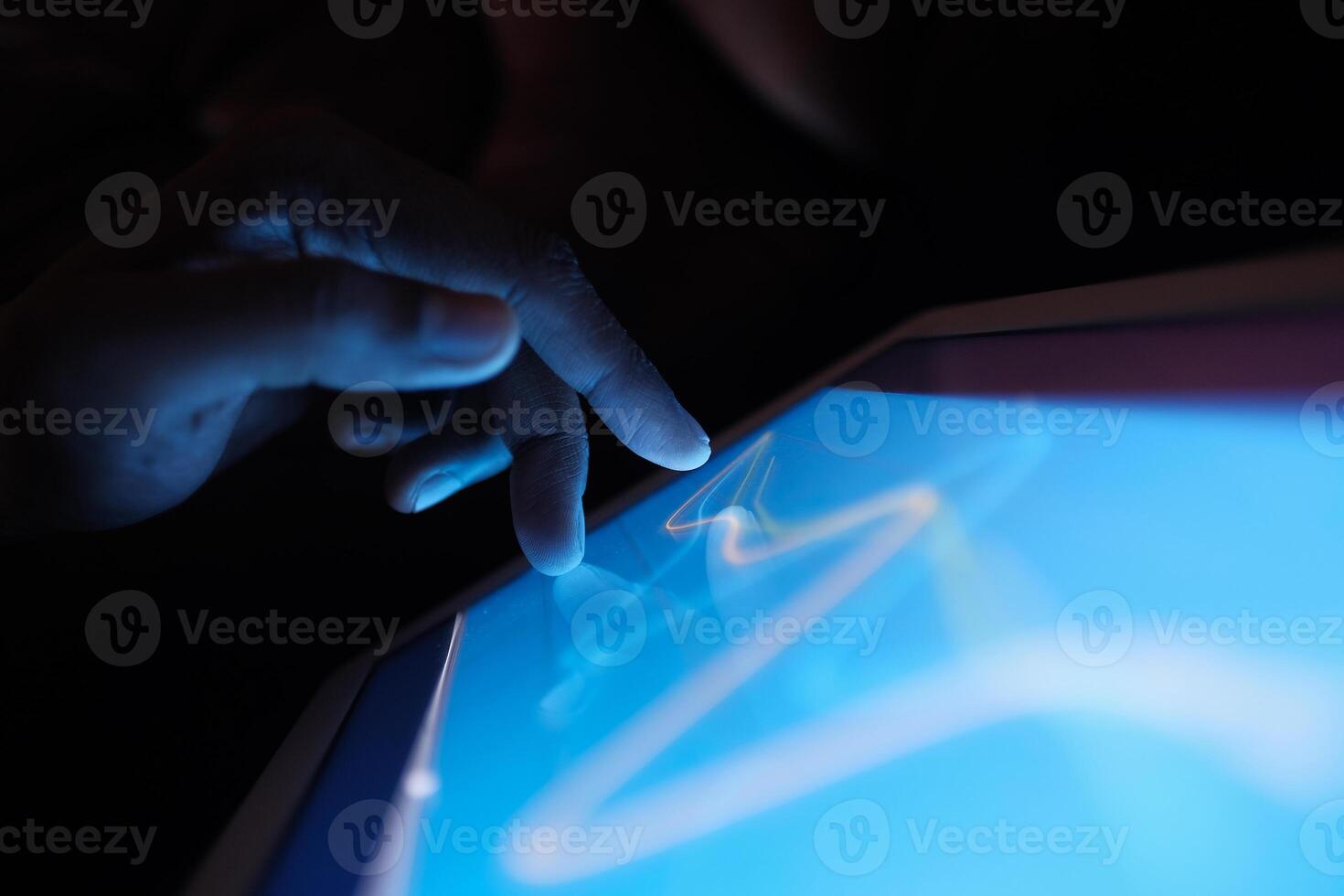 A finger gently touches an interactive tablet screen in low light, showcasing modern design photo
