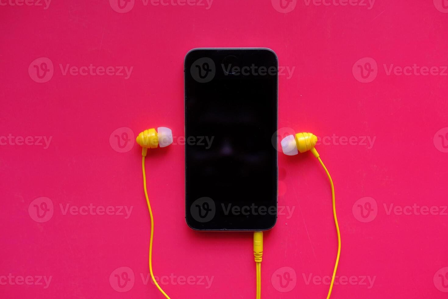 A trendy and stylish smartphone paired with bright yellow earbuds set against a pink background photo