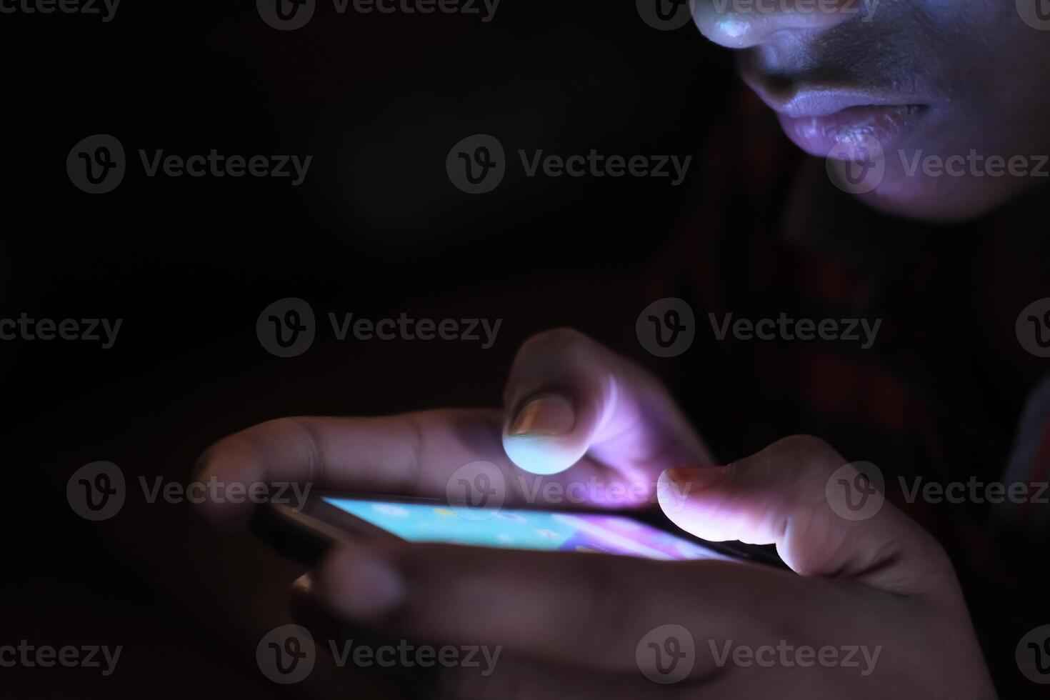 This image captures a closeup view of hands engaged with a smartphone amidst complete darkness photo