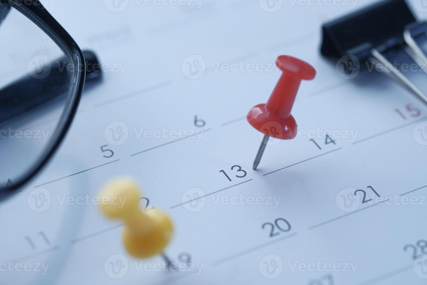 Brightly colored push pins affixed on a calendar, accompanied by a pair of reading glasses photo