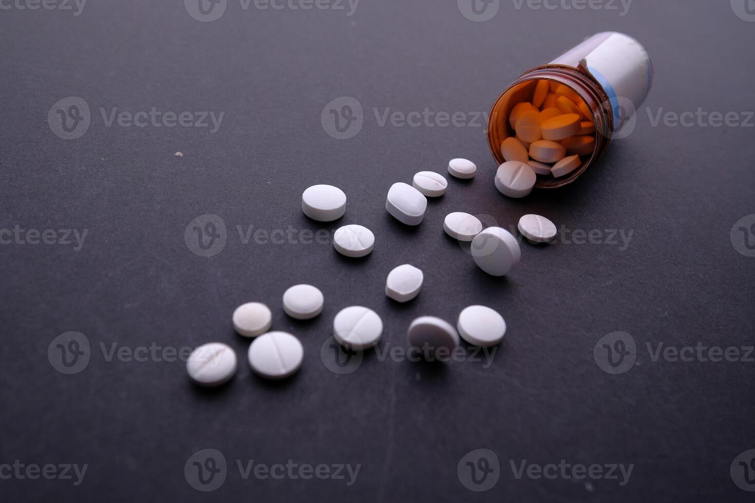 Numerous Scattered White Pills from an Open Prescription Bottle on a Black Surface photo