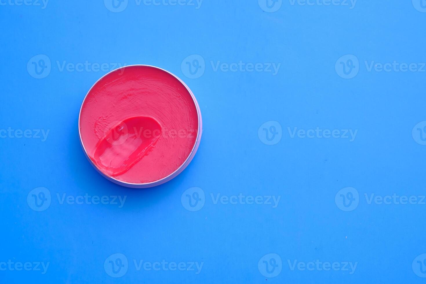 A vibrant pink cream beautifully displayed in a round container resting on a bright blue background photo