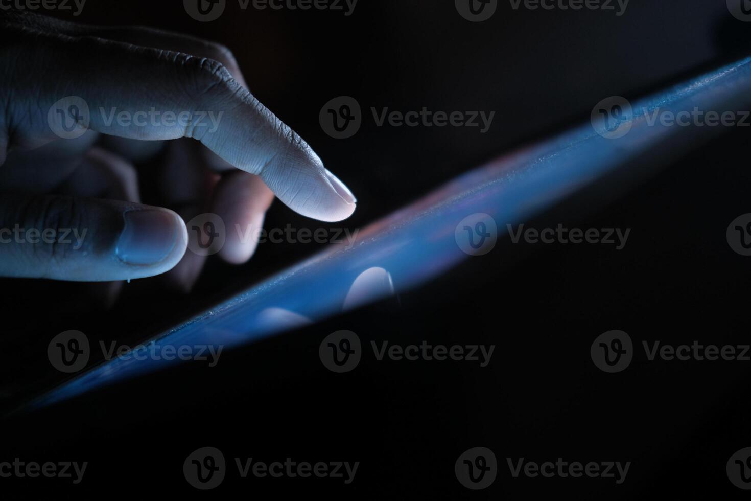 A closeup image showcases a hand actively interacting with a glowing tablet screen in the dim light photo