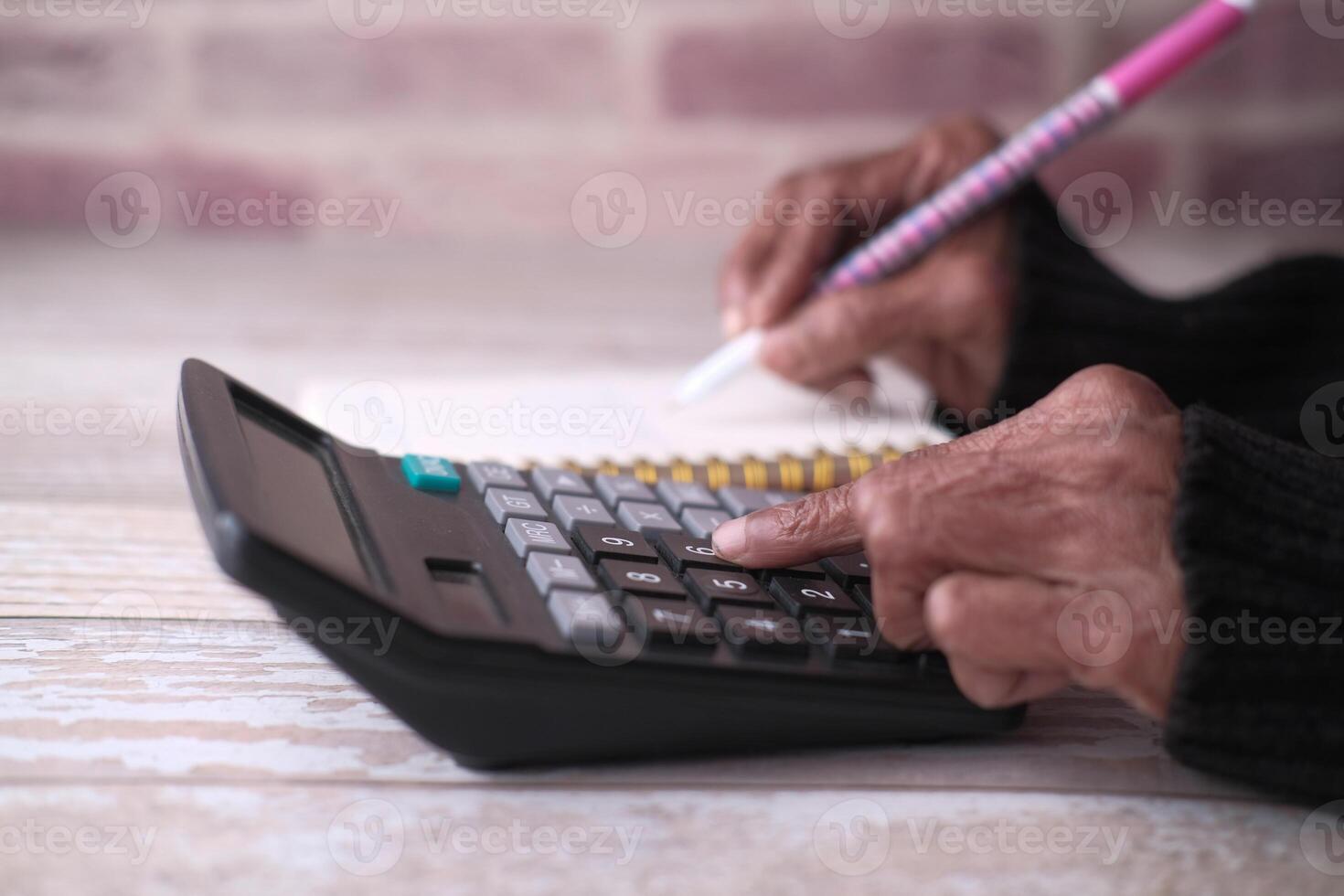 A Person is Actively Utilizing a Calculator While Also Taking Notes with a Pink Colored Pen photo