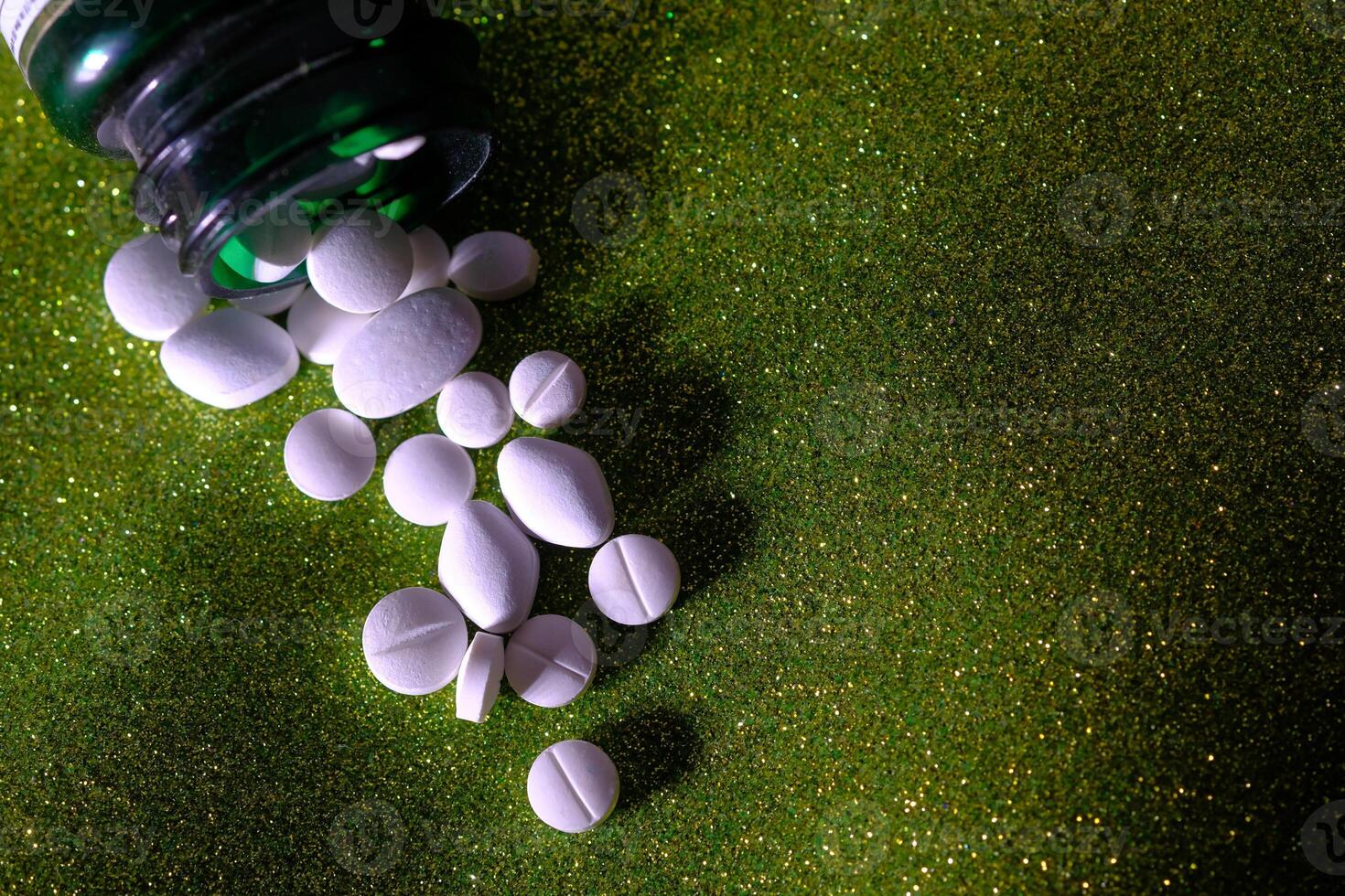 A mess of scattered pills along with a medicine bottle displayed prominently on a green background photo
