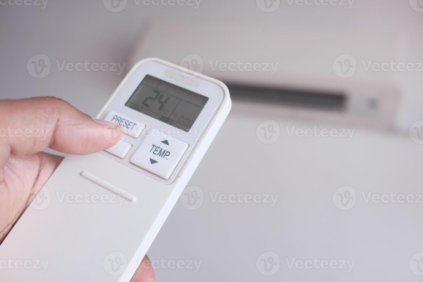 A hand is holding an air conditioner remote control that features a clear display for settings photo