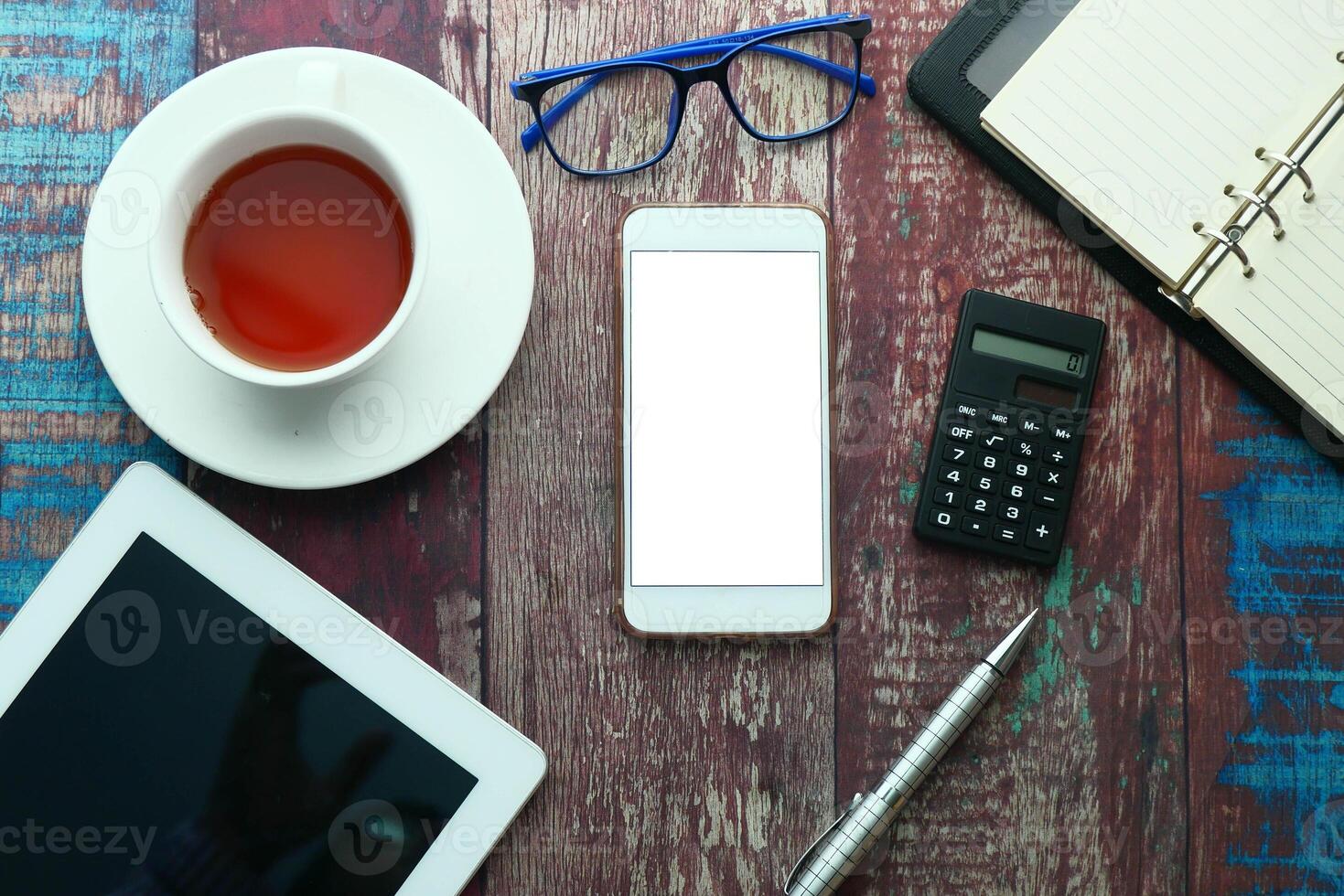 A wellarranged work desk setup featuring a mobile phone, a tablet, a calculator, and a cup of tea photo