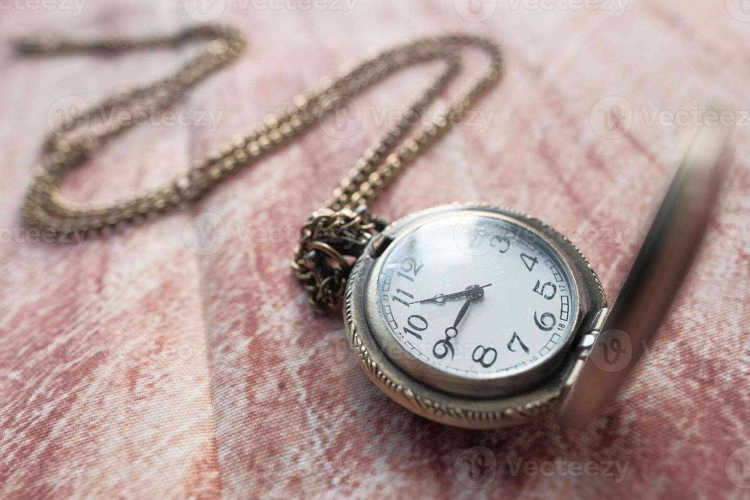 A Vintage Pocket Watch Complete with a Chain Resting on a Beautiful Wooden Surface photo