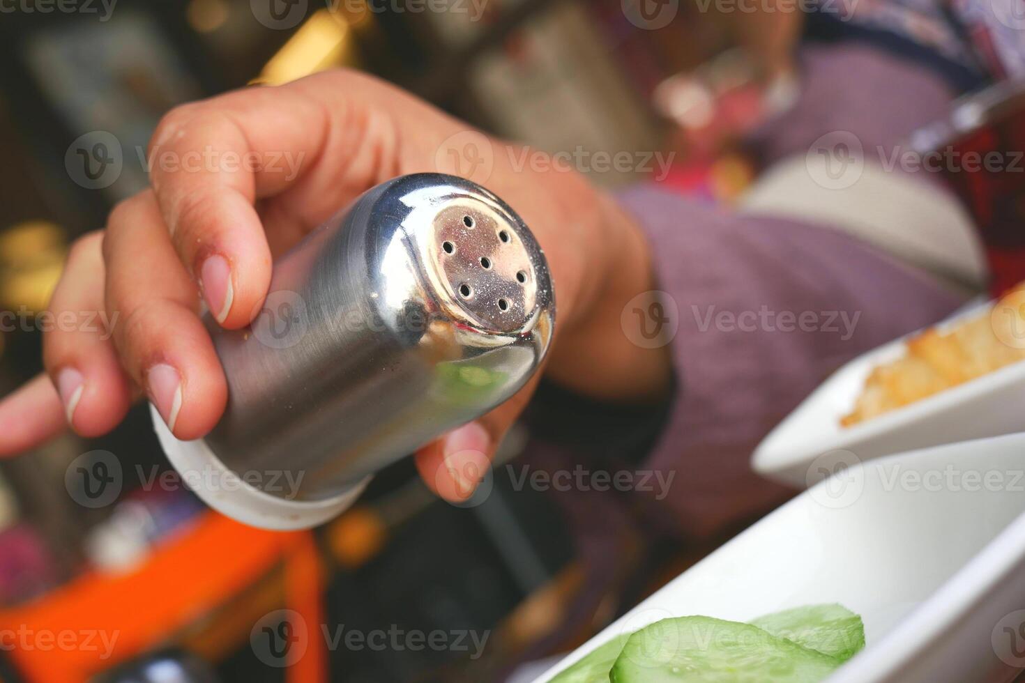 A person holding a salt shaker over a plate of food photo