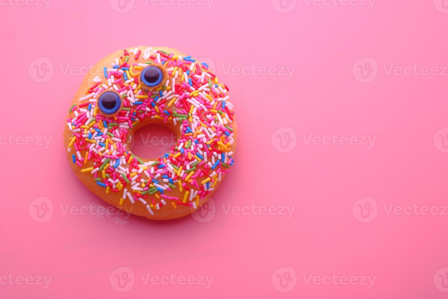 A colorful donut adorned with a variety of sprinkles set against a pink background photo